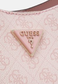 Rosa texturerat tyg med subtilt mönster, utrustat med en triangulär metallplatta i guldfärg med rosa accenter och präglingar i bokstäver.