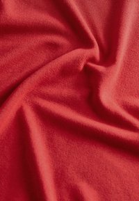 Tissu rouge à texture douce, présentant une surface lisse et légèrement réfléchissante ainsi qu'un léger stretch, disposé en plis délicats.