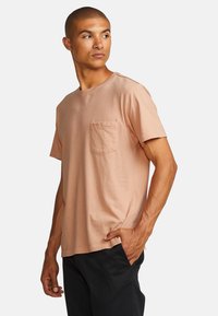 Short-sleeve t-shirt in light peach cotton. Features a left chest pocket and relaxed fit. Clean neckline and side seam detail.