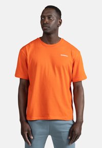 Orange bomulds t-shirt med rund hals og korte ærmer. Har et hvidt logo "ROSSIGNOL" på venstre brystområde. Flade sømme, afslappet pasform.