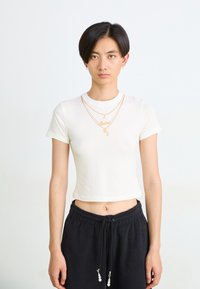 White short-sleeve crop top with round neckline, featuring gold lettering. Paired with black drawstring sweatpants with bead accents.