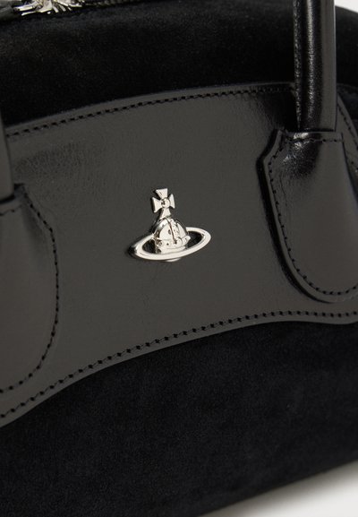Μαύρη δερμάτινη και σουέντ τσάντα χειρός με μια μικρή ασημί σφαίρα που έχει ένα έμβλημα σταυρού στο εμπρόσθιο πάνελ κοντά στη βάση του χερούλιου.