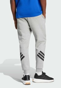 Gray sweatpants with black diagonal stripes on the lower legs, featuring an elastic waistband and cuffs, paired with black athletic shoes.