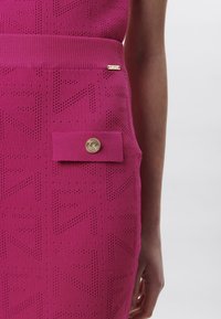 Fuchsia Strickrock mit einem gerippten Bund, versehen mit Logomuster und einer rechteckigen Tasche mit einem goldenen Knopfdetail.