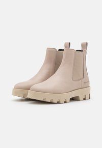 Botas Chelsea de cuero beige con suelas de goma gruesa, paneles laterales elásticos, lengüetas y un sutil logotipo en la zona externa del talón.