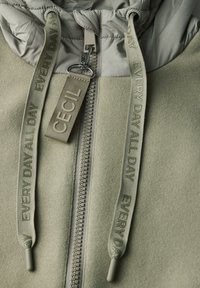 Giacca in pile verde con cappuccio trapuntato, zip bicolore e lacci con marchio che riportano il testo "Cecil" e "Every Day".