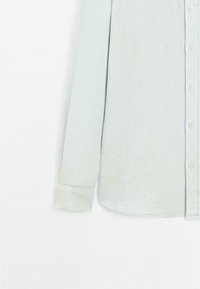 Chemise bleu clair à manches longues, boutonnée, en tissu doux. Elle présente un col et une fermeture à boutons sur le devant, avec des manches à boutonnière.