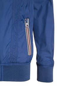 Modrá bunda se sukní a dolním torsem s žebrovaným manžetou a zapínací kapsou, která má červený, bílý a černý pruhovaný vzor.