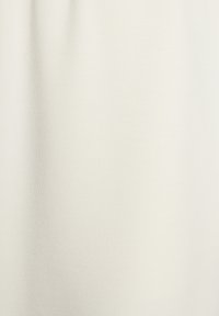 Hellbeige Stoff mit einer glatten, dehnbaren Textur. Das Material hat einen subtilen Glanz und eine feine Rippung, die eine gleichmäßige Oberfläche schaffen.
