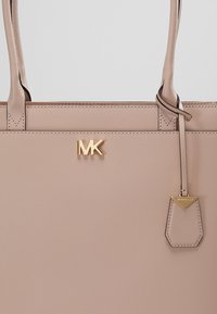 Sac à main en cuir beige avec logo MK doré et étiquette en cuir assortie suspendue à la poignée.