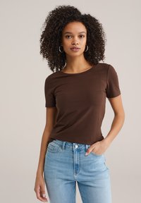 Bruin T-shirt met korte mouwen gemaakt van zacht, rekbaar materiaal. Getailleerd ontwerp met een ronde hals, gecombineerd met lichtblauwe jeans met een hoge taille.