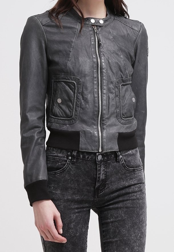 Donna che indossa una giacca di pelle nera aderente con cerniera e tasche con bottoni a pressione, abbinata a jeans neri a vita alta con effetto acid wash.