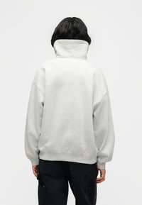 Γκρι φλις φούτερ με ψηλό γιακά, αποπερασμένους ώμους και ριμπ μανσέτες, φορεμένο με μαύρο παντελόνι. Απλό, μονόχρωμο χωρίς σχέδια.