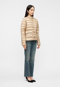 Μπεζ μπουφάν με οριζόντιες ραφές, ψηλό γιακά, κλείσιμο με κουμπιά και δύο μπροστινές τσέπες, σε συνδυασμό με μπλε τζιν και μαύρες γόβες.