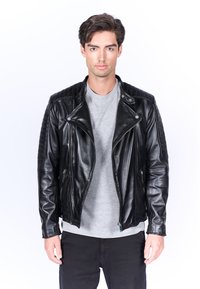 Giacca da moto in pelle nera con dettagli trapuntati sulle spalle, tasche con zip e hardware argento, abbinata a una maglietta grigia.