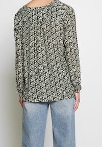 Blouse à manches longues dans un motif géométrique vert et crème, présentant une coupe décontractée, un col rond et des poignets élastiqués.