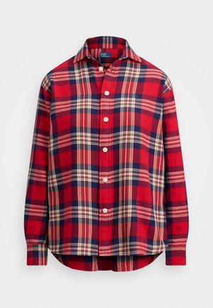 Red and navy plaid button-up shirt with a pointed collar, long sleeves, and curved hem. Features white buttons and a small branded logo.