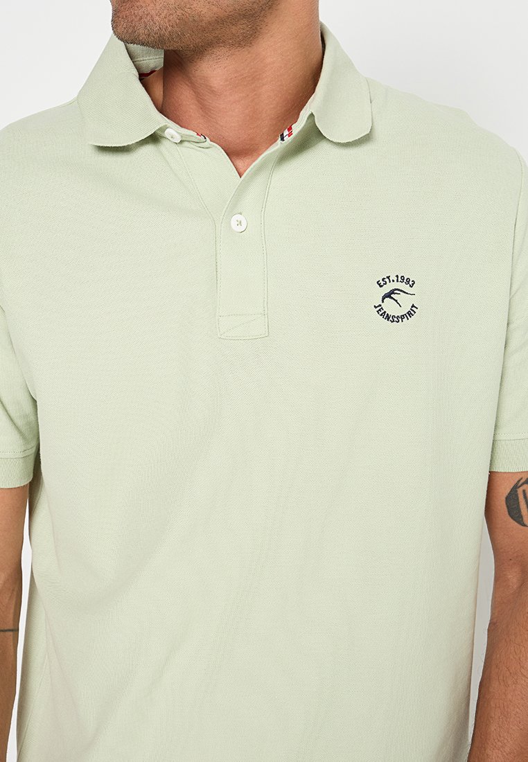 Hellgrünes Poloshirt aus strukturiertem Stoff, mit einem Kragen, zwei Knöpfen und einem kleinen gestickten Logo auf der Brust.