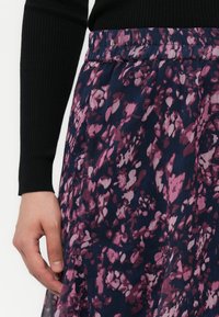 Nærbilde av en person som bærer et mørkt blomstrete skjørt med rosa og lilla mønstre, kombinert med en svart rillelangermet topp.