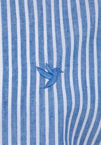 Niebiesko-biała tkanina w paski z wyszytym niebieskim kolibrkiem. Tekstura wydaje się gładka z tkanym wzorem.