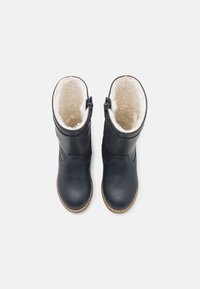 Bottes en cuir marine avec une douce doublure en fausse fourrure blanche, hauteur mi-mollet, et une fermeture éclair décorative sur le côté. Bout rond et semelle contrastante.