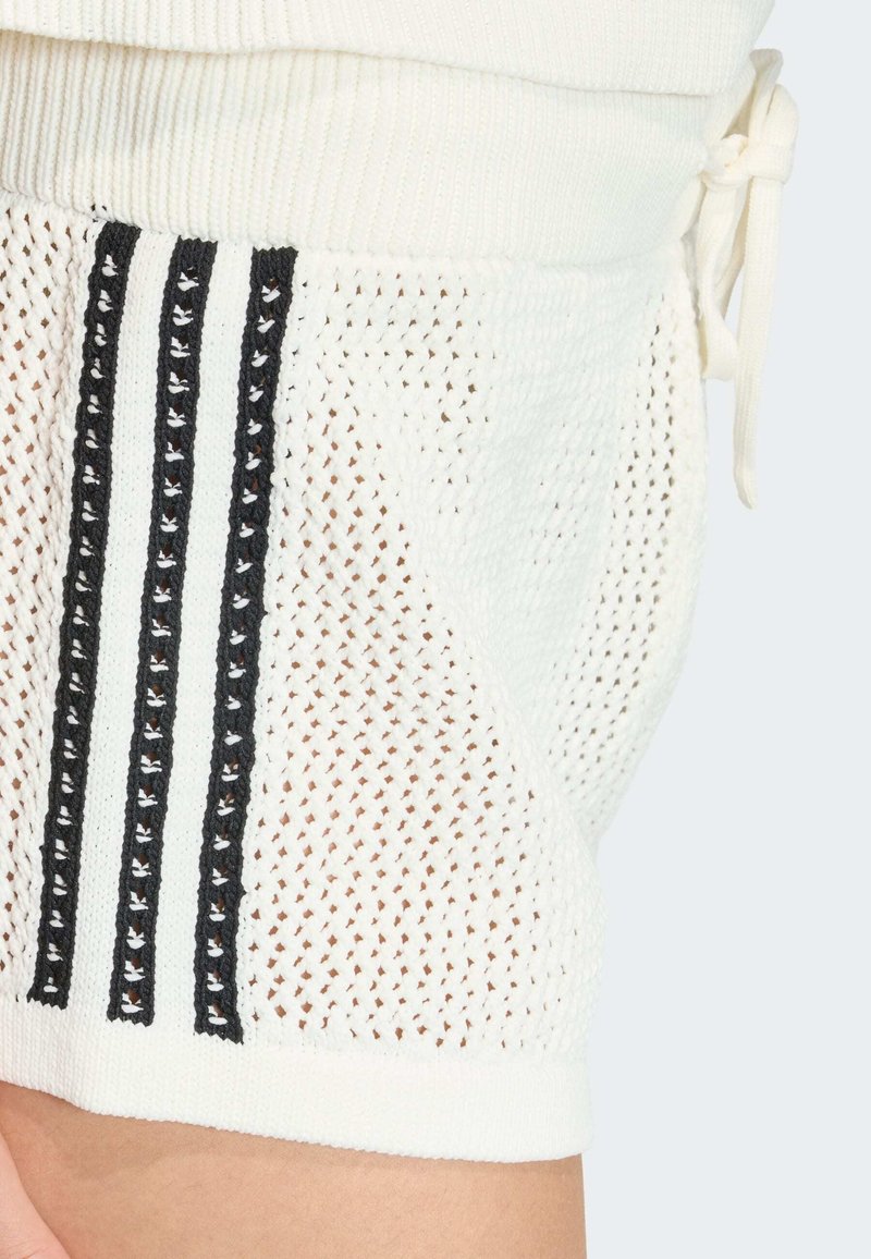 Shorts bianchi lavorati a maglia con una texture a rete e strisce verticali nere. Caratterizzati da una vita con coulisse e polsini a coste.