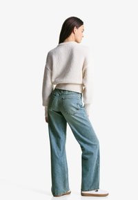 Afskåret cremefarvet sweater med en tekstureret finish, parret med lyseblå højtaljede jeans og hvide sneakers med brune såler.