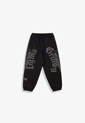 Czarne spodnie dresowe ze ściągaczami na nogawkach i w pasie, z szarym gotyckim napisem „Grimey” oraz grafiką skrzydeł na przednich nogawkach.