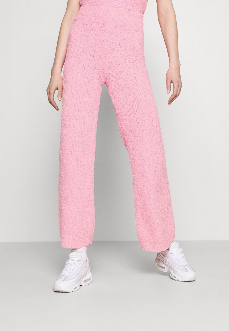 Różowe dzianinowe spodnie z szerokimi nogawkami o teksturowanym wykończeniu i wysokim stanie, w połączeniu z białymi sneakersami. Charakteryzuje się luźnym i swobodnym krojem.
