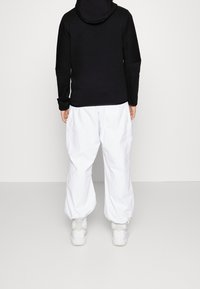 Sudadera negra con capucha, combinada con pantalones cargo blancos de corte holgado. Se ven zapatillas blancas en la parte inferior.