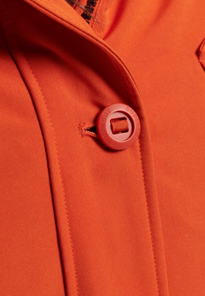 Oranje jas met een grote, ronde knop met een vierkante opening, gladde textuur en strakke lijnen in het ontwerp.