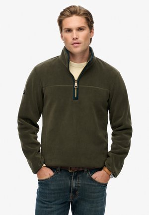 Donkergroene fleecepullover met een halve rits, met een contrasterende binnenste kraag, een gladde textuur en een naaddetail op de borst.