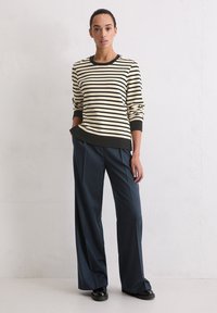 Gestreepte pullover in beige en zwart, gecombineerd met ruime marineblauwe broeken. Glad textuur en ribgebreide manchetten, met een casual pasvorm.