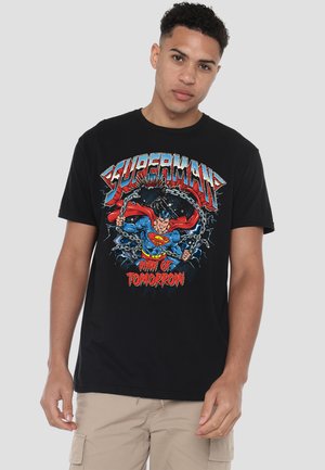 Young man wearing black Superman T-shirt with comic-style graphic of Superman breaking chains and text "Man of Tomorrow."