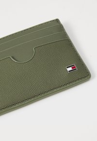 Green leather cardholder featuring multiple card slots, textured surface, and a small logo emblem in red, white, and blue colors.