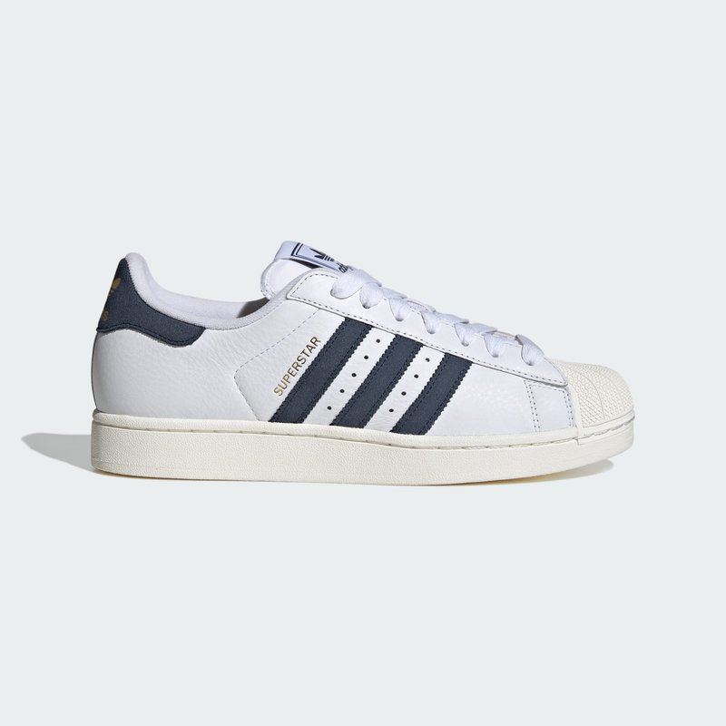 White Adidas Superstar sneaker with black stripes, rubber shell toe, and gold "Superstar" text on leather side panel.