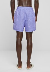 Shorts de bain violet clair avec un motif décoratif, taille élastique, poches latérales et coupe décontractée. Texture lisse et design décontracté.