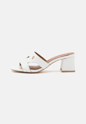 Sandalias de tacón blancas con textura de cocodrilo, diseño de punta abierta y detalle de tiras cruzadas. Tacón cuadrado de bloque y plantilla color beige.