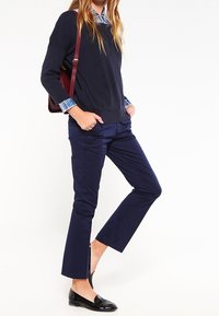 Granatowy sweter dzianinowy o prążkowanej fakturze, zestawiony z granatowymi spodniami slim-fit. Widoczne czarne lakierowane loafersy i mankiety koszuli w kratę.