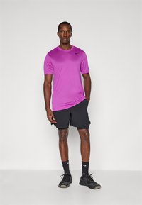 Lila Sport-T-Shirt mit kurzen Ärmeln, schwarze Shorts, schwarze Socken und schwarze Sportschuhe mit strukturiertem Finish und minimaler Markenkennzeichnung.