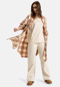 Beige plaid shirt over cream T-shirt, wide cream pants, and brown slip-on shoes. Accessories include black sunglasses. Textured fabric details visible.