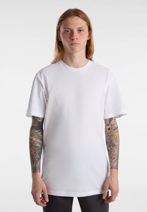Hvid bomulds T-shirt med rund hals, korte ærmer og en afslappet pasform, vist på en person med synlige tatoveringer på armene.