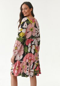 Blumenkleid mit großen rosa und weißen Blumen auf schwarzem Hintergrund; lange Ärmel, gestufter Rock und weicher Stoff.