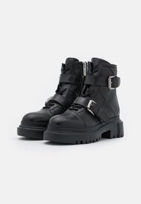 Stivaletti neri in pelle con suola spessa, dotati di due cinghie con fibbie metalliche, una zip laterale e suola in gomma texturizzata.