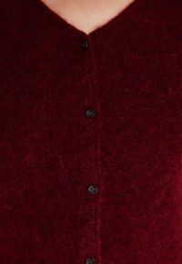 Burgundy knit cardigan with a V-neck, featuring six black buttons down the front and a soft, textured, fuzzy fabric.