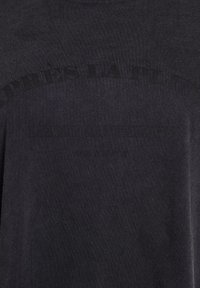 Sort t-shirt i sort bomuldsstof med et stort, mørkt tekstgrafik med "Après la pluie" trykt hen over fronten i en buet form.