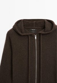 Brown cardigan featuring a hood, knit texture, front zipper closure, and subtle variations in color. Made from 100% cashmere.