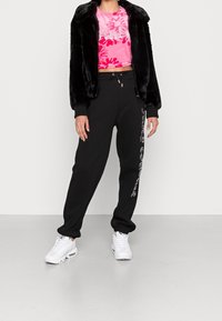 Svart bomberjacka i konstpäls, rosa blommig crop top, svarta sweatpants med vit text och vita sneakers. Släta material och avslappnad passform.