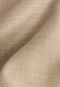 Beige tkanina s jemnou texturou, s jemným a těsným vzorem tkaní. Světlo se na jejím povrchu jemně odráží.