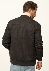 Schwarze täuschend echte Leder-Bomberjacke mit gerippten Bündchen und Saum, ausgestattet mit einer glatten Textur und einem schlichten, klaren Design.